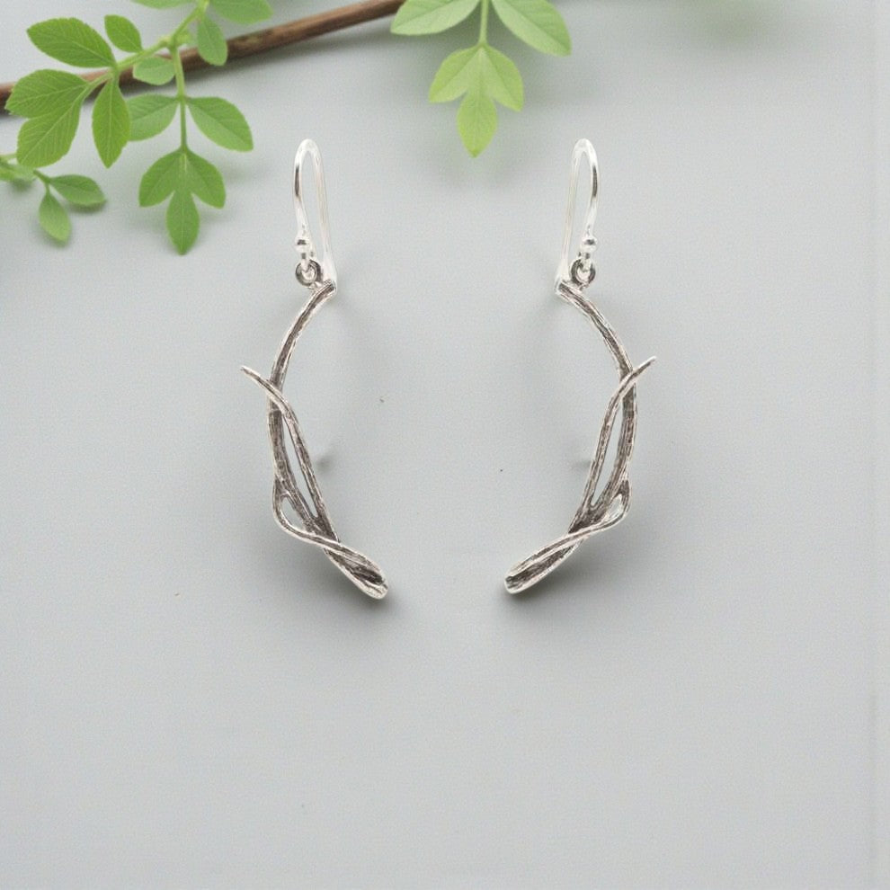 Silver branch-shaped earrings on a light gray background with green leaves.